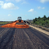 Un bulldozer répand du sable sur une géogrille Basetrac Grid posée pour le renforcement de la couche de base sur un chantier de construction