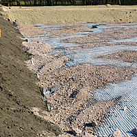 Géogrille Basetrac Grid sur un chantier, sur laquelle du sable ou du gravier a déjà été partiellement répandu