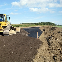 Un bulldozer répand de la terre sur une grille Basetrac déjà posée sur le chantier