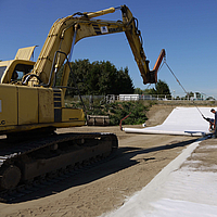 L'excavateur utilise une traverse de pose pour dérouler les nattes de bentonite Tektoseal® Clay