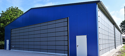 Façade pliante Lubratec sur un terrain de football couvert Grande porte pliante Lubratec à l'avant d'une salle de soccer bleue
