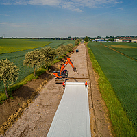 Vue aérienne montrant l'excavatrice et la traverse de pose lors de la pose de géotextiles Stabilenka