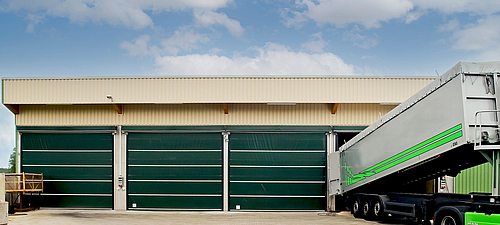 Lubratec Stabidoor Trois portes de garage Lubratec vertes fermées sur un entrepôt beige. Un camion est en train d'être déchargé à la porte ouverte de droite.