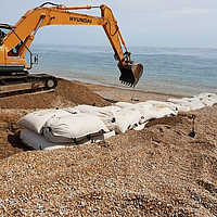 Installation de SoilTain Bags sur une plage de galets avec une pelleteuse pour la protection contre les inondations