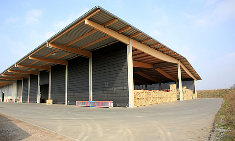 Grand entrepôt avec façade ouverte et avancée de toit. Le côté long est fermé par six façades pliantes grises